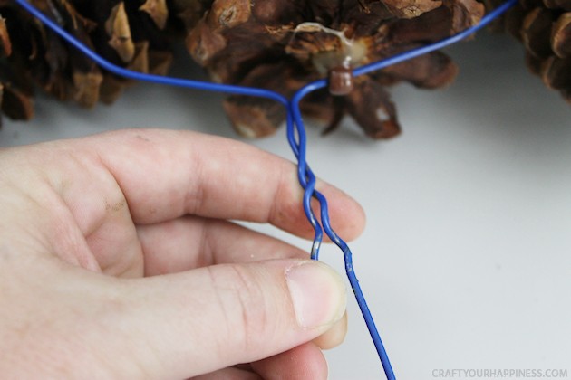 Learn how to make a pinecone wreath in 30 minutes! You can decorate the base wreath however you wish. We used a big red bow. Plus it's an upcycle project!