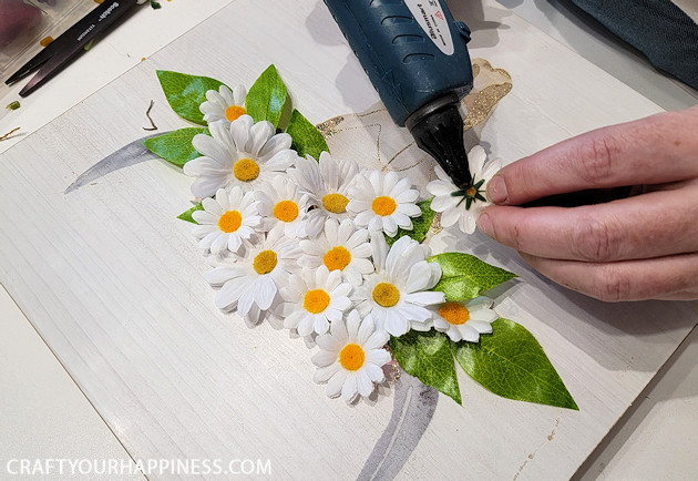 If you have old artwork that no longer fits your home decor here's a quick fun way to update it with a simple 3D painting makeover! Some artificial flowers and a hot glue gun is all we used!
